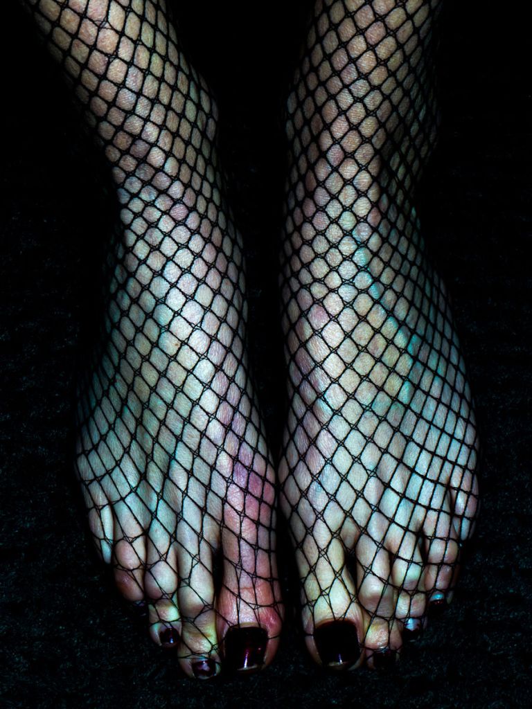 Des pieds serrés l'un contre l'autre, dans un collant résille, image prise avec un flash dans l'obscurité