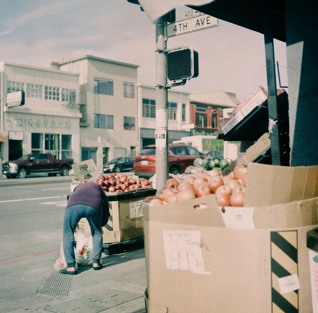 Sur le trottoir, une personne installe ses étalages de fruits. 