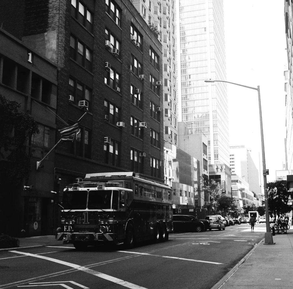 Un camion de pompier est arrêté à un feu rouge. La photographie est en noir et blanc.