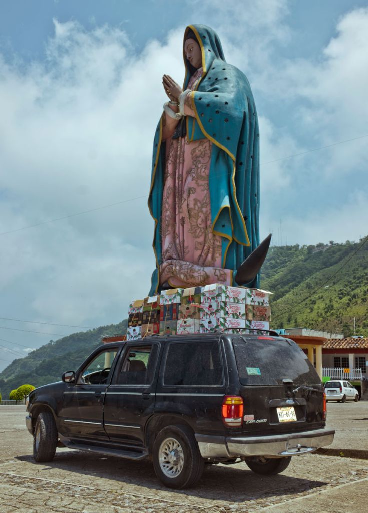 Une photographie d'une voiture qui passe à côté d'une statue de Vierge Marie par Cristina de Middel