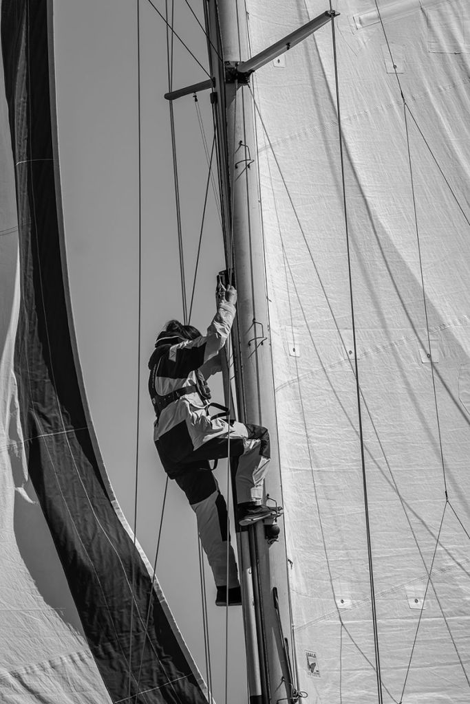 Photographie en noir et blanc de Garance Madelénat montrant une femme grimpant au mât d'un voilier.