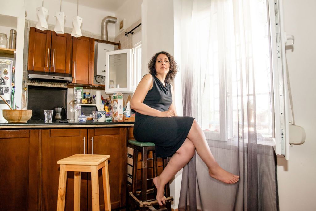 Une femme pose dans son appartement assise sur un tabouret