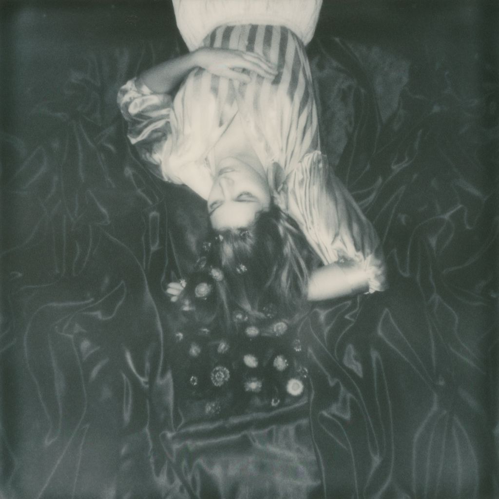 Polaroïd en noir et blanc, portrait de la musicienne Claire Days, allongée au milieu de l'herbe.