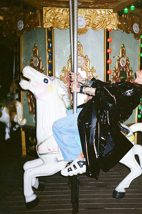 Une personne en long manteau noir est assise sur un cheval de carrousel en action.