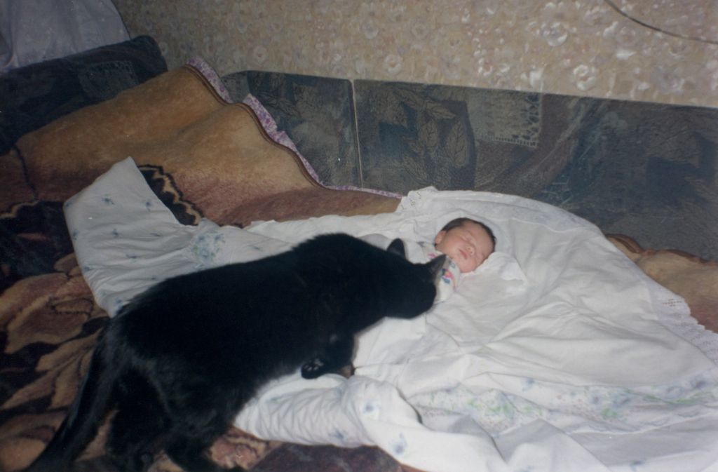 Un bébé et un chat noir dans un lit.