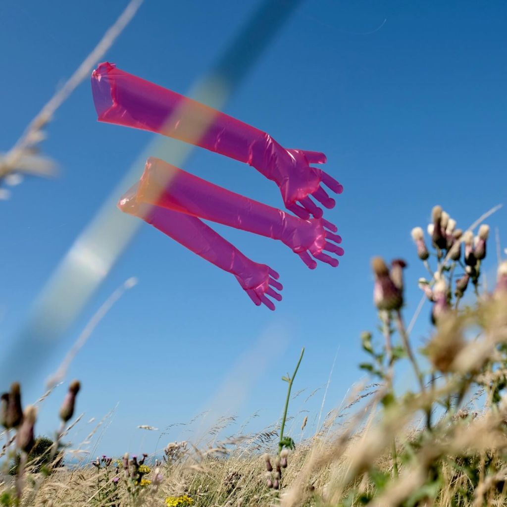 Des gants en vinyle rose fluo volent au vent dans une prairie.