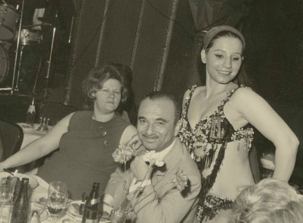 Photographie montrant un couple, aux côtés d'une danseuse, au restaurant dans les années 1960-1970.