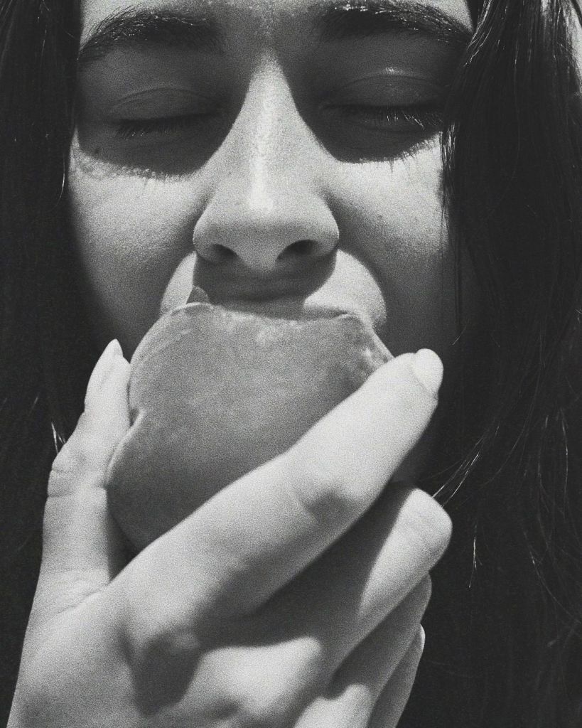 Photo en noir et blanc. Gros plan sur un visage qui croque dans une pêche.