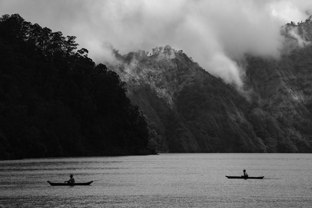 Image en noir et blanc de paysage. Deux pirogues traversent un lac au bord des montagnes