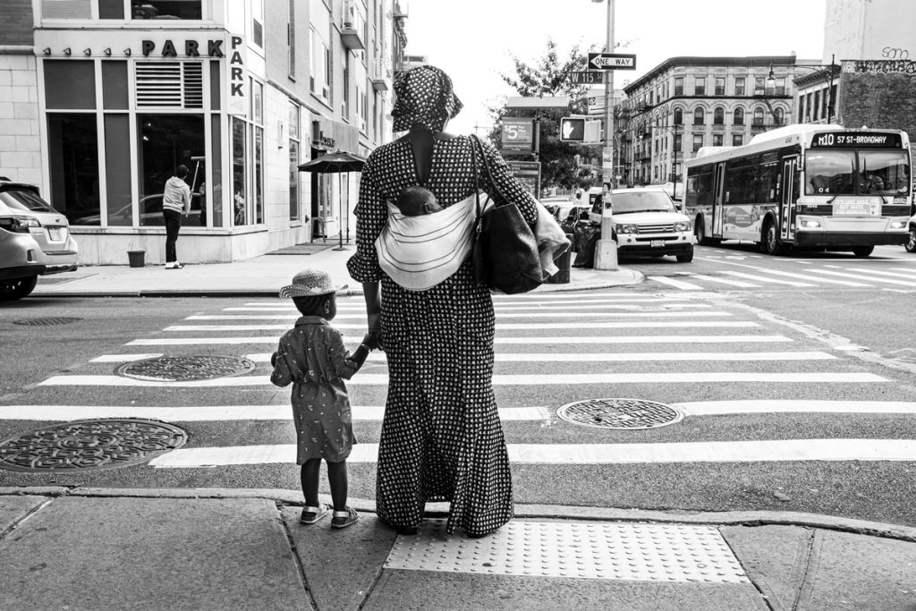 Photographie en noir et blanc de Kate Sterlin montrant une femme dans la rue avec ses enfants, dont l'un est sur son dos